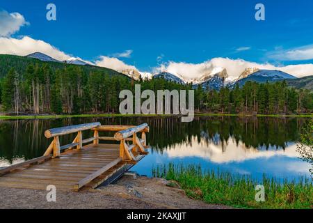 A view of Sprague Lake in the Rocky Mountains, surrounded by green trees and mountains reflecting in the water Stock Photo