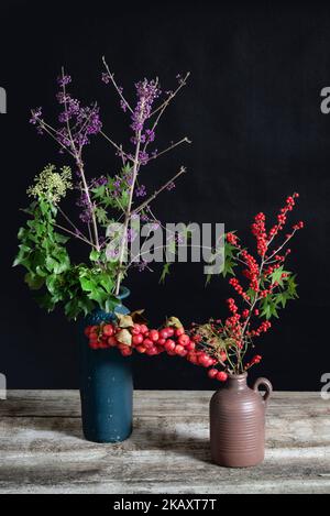 Callicarpa and Hedera helix and Ilex in blue and brown vases. Stock Photo