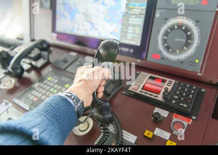 Navigational control panel and VHF radio with hand. Radio communication at sea. Working on the ship's bridge. Stock Photo