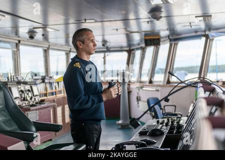 Deck officer with binoculars on navigational bridge. Seaman on board of vessel. Commercial shipping. Cargo ship. Stock Photo