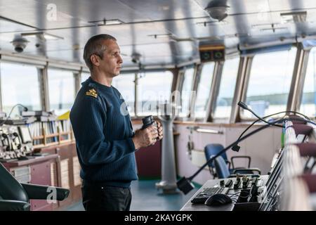 Deck officer with binoculars on navigational bridge. Seaman on board of vessel. Commercial shipping. Cargo ship. Stock Photo