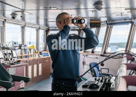 Deck officer with binoculars on navigational bridge. Seaman on board of vessel. Commercial shipping. Cargo ship. Stock Photo