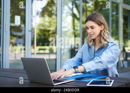 Portrait of businesswoman working with laptop. Corporate woman using computer outdoors, attend video chat meeting while sitting outside office Stock Photo