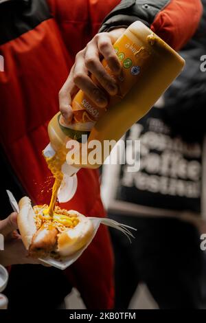 Close up someone pouring mustard onto their hotdog, sausage on a roll, sausage in a BAP with onions mustard Stock Photo