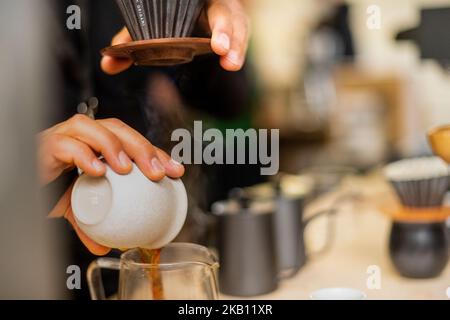 Close up someone pouring coffee filter in one hand cup in the other other bits of coffee making blood in the background Stock Photo