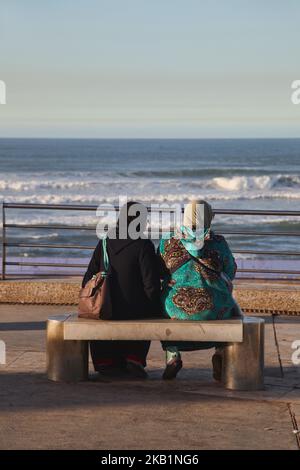 Muslim women relax on a bench by the Atlantic Ocean along the Cornish in Casablanca, Morocco, Africa. The Cornish of Casablanca is a beautiful stretch along the Atlantic coast. The serpentine road has a parallel walkway for the pedestrians and there are a number of hotels, restaurants, and nightclubs located along the Cornish. (Photo by Creative Touch Imaging Ltd./NurPhoto) Stock Photo