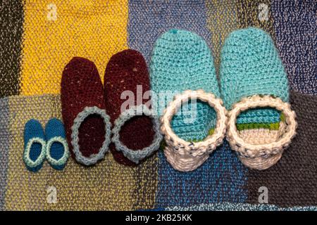 Warm, handmade, colorful woolen slippers for the whole family on soft, knitted background Stock Photo