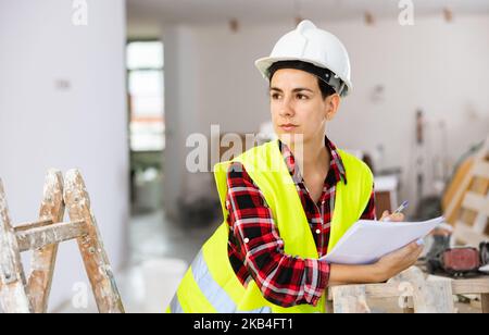 Focused young female civil engineer making notes at construction site indoors Stock Photo