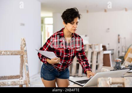 Woman builder checking project documentation and using laptop while working Stock Photo