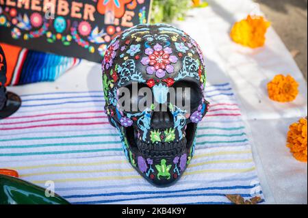 A colorful painted skull with marigold flowers and a Remember Me sign in the background are on an altar area as part of a Dia de los Muertos festival Stock Photo