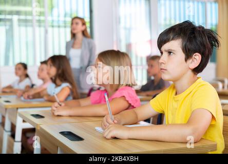 Focused preteen schoolboy writing in workbook at lesson in classroom Stock Photo
