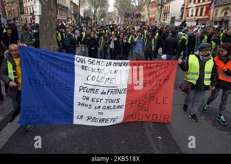 Two Yellow Vests protesters wave a giant French Flag. For the Act XI of the Yellow Vest movement, more than 10 000 people took to the streets of Toulouse for the anti-governement protest. Skirmishes took place between protesters and riot police during 3 hours. Riot police used of tear gas canister and one police water cannon. The Yellow Jackets movement begun on November 17th by a protest against the rise of taxes on oil products. The rise of taxes was the detonator of their wrath against French President Macron and his governement and their demand of his resignation.Toulouse. France. January  Stock Photo