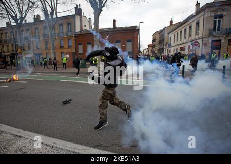 A protester throws back a tear gas canister to riot police. For the Act XI of the Yellow Vest movement, more than 10 000 people took to the streets of Toulouse for the anti-governement protest. Skirmishes took place between protesters and riot police during 3 hours. Riot police used of tear gas canister and one police water cannon. The Yellow Jackets movement begun on November 17th by a protest against the rise of taxes on oil products. The rise of taxes was the detonator of their wrath against French President Macron and his governement and their demand of his resignation.Toulouse. France. Ja Stock Photo