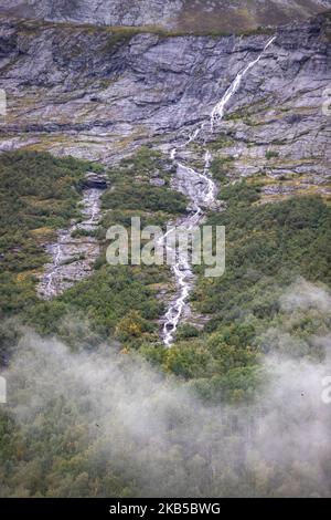 Beautiful waterfalls inside intense nature in dramatic scenery with clouds or green forest natural environment, seen at the fjords in Norway with forests and steep mountains. Water coming from high altitude mountain peaks and glaciers ending up throughValldola river to the fjords and the sea at the area of Valldal and Valldalen valley on 31 August 2019. (Photo by Nicolas Economou/NurPhoto) Stock Photo