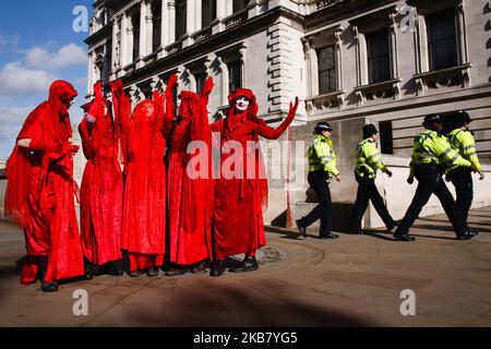 Police officers walk past members of environmentalist performance art troupe the Red Rebel Brigade on Horse Guards Road as members of climate change activist group Extinction Rebellion (XR) take part in the second day of the group's 'International Rebellion' in London, England, on October 8, 2019. By early Tuesday evening the Metropolitan Police were reporting that a total of 531 arrests had been made over the two days of protests in the city so far, with police officers working to clear people and tents from many of the sites taken over by activists yesterday. Similar blockades by Extinction  Stock Photo