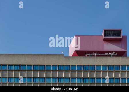 Outdoor exterior side view of typical modern office building with rooftop extension with red aluminium cladding geometric shape against blue sky. Stock Photo