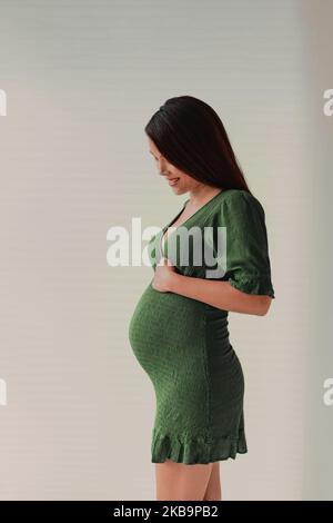 Pregnancy photoshoot beautiful pregnant woman model profile wearing dress to show baby bump on maternity shoot. Vertical portrait in studio Stock Photo