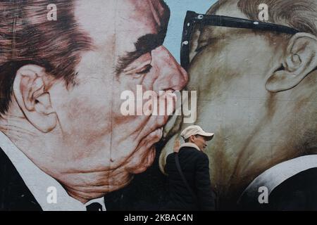 An Asian visitor poses for a picture near a mural by Russian artist Dmitri Vrubel ‘My God, Help Me to Survive This Deadly Love’, commonly known as ‘Fraternal Kiss’ that shows former Soviet Union leader Leonid Brezhnev kissing former east German leader Erich Honecker at a still-standing section of the former Berlin Wall called the East Side Gallery, seen on the eve of the upcoming 30th anniversary of the fall of the Berlin Wall. On Friday, November 8, 2019, in Berlin, Germany. (Photo by Artur Widak/NurPhoto) Stock Photo