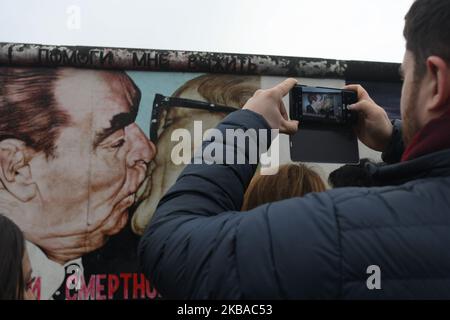 A visitor takes a picture of a mural by Russian artist Dmitri Vrubel ‘My God, Help Me to Survive This Deadly Love’, commonly known as ‘Fraternal Kiss’ that shows former Soviet Union leader Leonid Brezhnev kissing former east German leader Erich Honecker at a still-standing section of the former Berlin Wall called the East Side Gallery, seen on the eve of the upcoming 30th anniversary of the fall of the Berlin Wall. On Friday, November 8, 2019, in Berlin, Germany. (Photo by Artur Widak/NurPhoto) Stock Photo