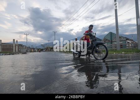 The driver pushed his motorcycle through the tidal flood in Kampung Lere, Palu, Central Sulawesi, Indonesia, on November 27, 2019. The high tide caused residents' houses in the area to be flooded. The condition was exacerbated by land subsidence as high as 1.5 meters due to the earthquake on 28 September 2018 then. (Photo by Basri Marzuki/NurPhoto) Stock Photo