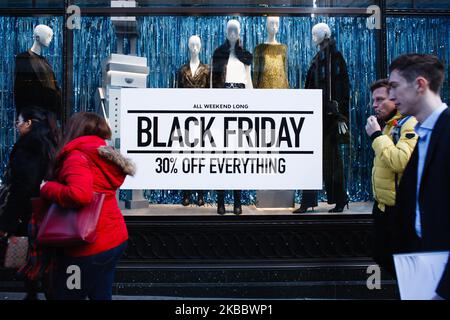 People walk past a sign advertising Black Friday discounts at a clothing store on Regent Street in London, England, on November 29, 2019. (Photo by David Cliff/NurPhoto) Stock Photo