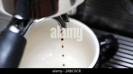 A close up view of the portafilter tip delivering the first few drips from the perfect espresso coffee pour into a black handled cup. Stock Photo