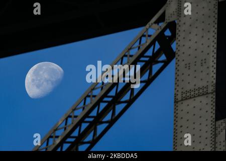 The moon through Williamsburg Bridge, a suspension bridge in New York City across the East River, connecting the Lower East Manhattan with Williamsburg neighborhood in Brooklyn, at Broadway. The illuminating Luna, earth's natural satellite in orbit, as seen at the Waning gibbous, lunar calendar phase, with 76% visible. NYC, USA - November 17, 2019 (Photo by Nicolas Economou/NurPhoto) Stock Photo