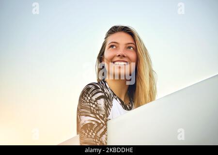 Its a beautiful day for a surf. Low angle shot of an attractive young female surfer standing with her surfboard on the beach. Stock Photo