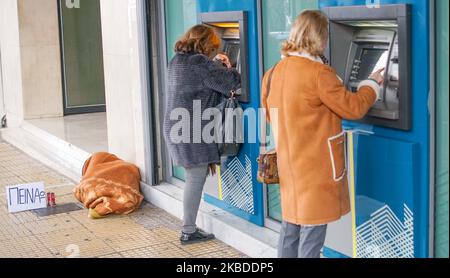 A homless man lays on the floor as beggings for some money outside a branch of National Bank of Greece as people withdrawn money from a cashpoint , in Athens , Greece , 23 December 2019. (Photo by Giannis Alexopoulos/NurPhoto) Stock Photo