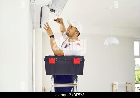 Worker with toolbox standing on ladder and installing modern air conditioner on wall Stock Photo