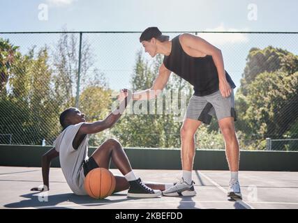 Sports, teamwork and men with helping hand in basketball, player giving support, help and assistance. Fitness, friends and man lifting black man with Stock Photo