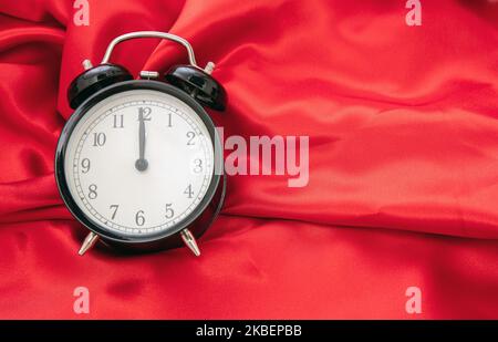 Black retro alarm clock on red satin background top view, copy space. Stock Photo
