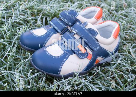 fashionable white leather sneakers of the boy on the frosty grass Stock Photo