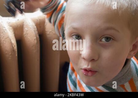 boy basking near old cast iron radiator in room Stock Photo