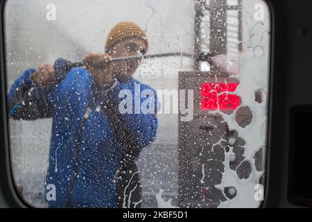 A man washes a car from a hose behind the car window Stock Photo