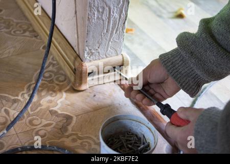 man twists the skirting board with a screwdriver on the floor Stock Photo