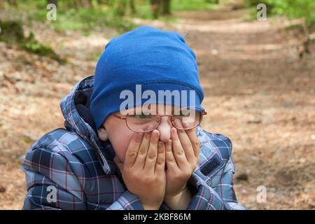 boy in glasses covers his face with his hands in autumn Stock Photo