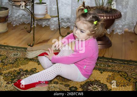Girl trying on and wearing her mother's red shoes on her feet Stock Photo