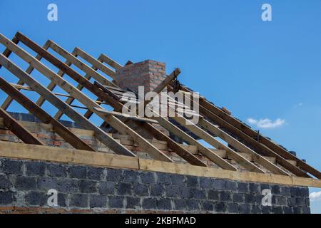 A new build roof with a wooden truss framework making an apex against a blue sky with cloud. Stock Photo
