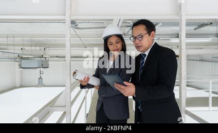 Female engineer in hardhat hold the construction plan while looking at tablet computer on the building inspector hand. Lighting and air conditioning p Stock Photo