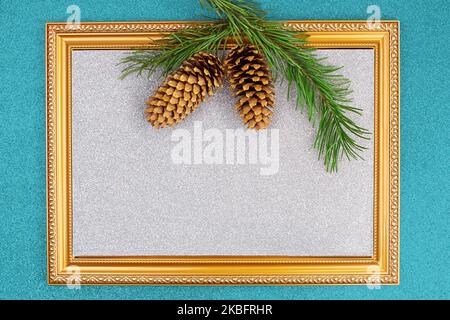 Golden frame with sparkling silver backdrop with spruce branch and cones on blue shiny background. Christmas, New Year. Copy space Stock Photo