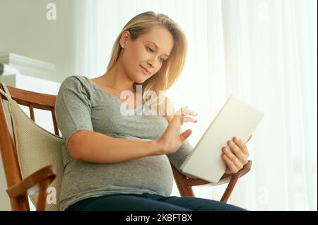 Getting a better understanding of her pregnancy. a pregnant woman using her digital tablet while sitting on a rocking chair. Stock Photo