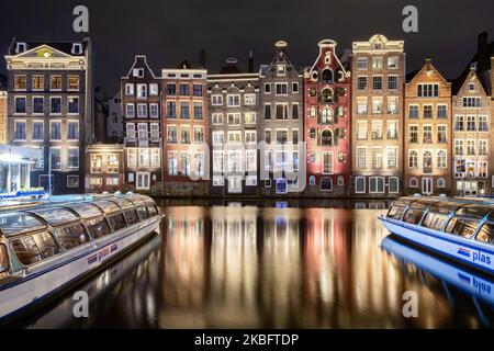 The famous colorful dancing houses with authentic Dutch architecture, lining traditional buildings with lights. The illuminated houses over the water at Damrak Canal basin are a famous tourist attraction, a landmark near the central train station, an important tourism attraction, at Amsterdam, Holland, the Netherlands as seen after sunset, during the magic blue hour, dusk and night. Amsterdam, Netherlands (Photo by Nicolas Economou/NurPhoto) Stock Photo