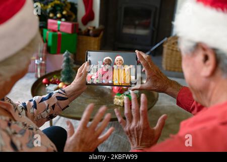 Senior caucasian couple with santa hats having video call with happy diverse couple Stock Photo
