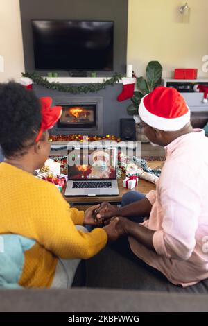 African american couple with santa hats having video call with santa claus with face mask Stock Photo