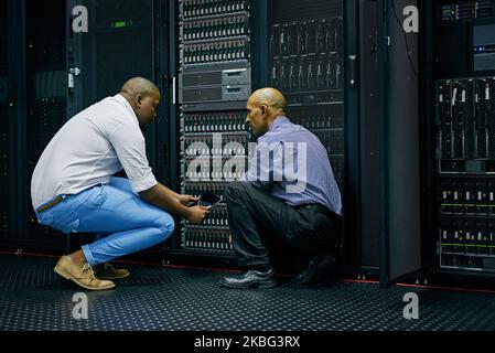 Working efficiently to resolve the issue. two IT technicians repairing a computer in a data center. Stock Photo
