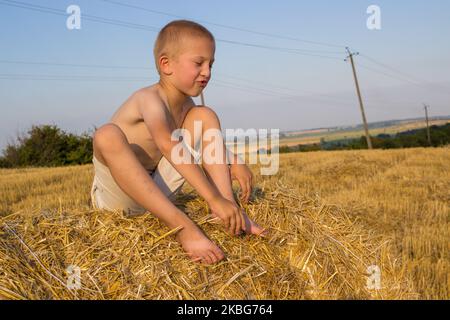 the last day of summer, the boy rejoices during holidays in the field sitting on a bale of hay Stock Photo