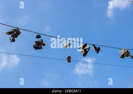 Silhouettes of shoes hanging on cable against sky. Stock Photo