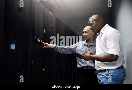 Essential equipment. two IT technicians using a digital tablet while working in a data center. Stock Photo