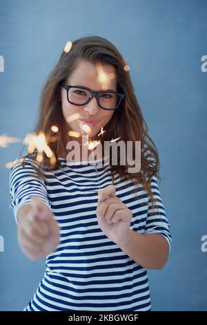 Dont you dare dim your light to make others comfortable. Studio shot of a beautiful young woman holding sparklers against a blue background. Stock Photo